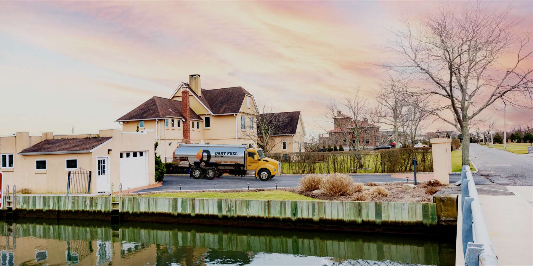 Residential heating oil truck with a peach stucco home alongside a canal at sunset in Saint James, Long Island, New York delivering fuel oil. Residential heating oil truck with a peach stucco home alongside a canal at sunset in Saint James, Long Island, New York delivering fuel oil.